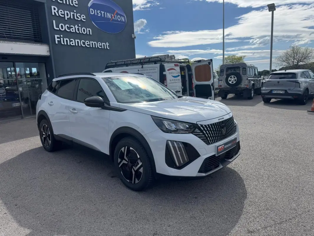 Vue 3/4 avant droit d’un Peugeot 2008 blanc 2024 avec barres de toit et jantes alliage noires.