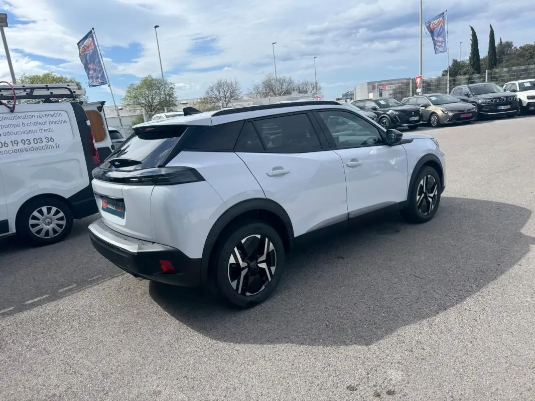 Peugeot 2008 blanc vue 3/4 arrière droit, avec barres de toit noires et jantes alliage 17 pouces.