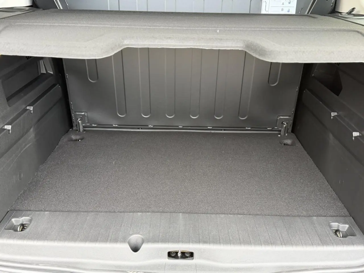 Coffre spacieux du Peugeot Rifter gris acier, vue arrière ouverte avec cache-bagages déployé.