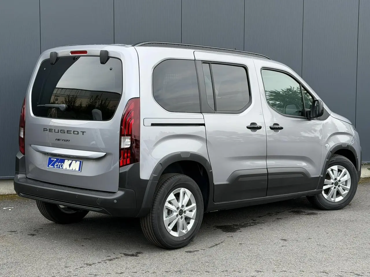 Peugeot Rifter gris acier vu en 3/4 arrière droit, avec portes coulissantes et vitres arrière surteintées.