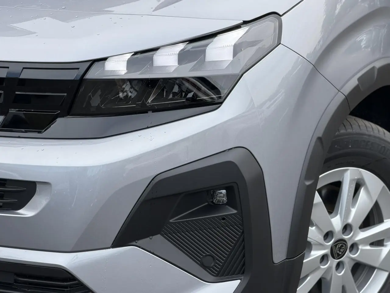 Gros plan sur l’avant droit du Peugeot Rifter gris acier 2026, mettant en valeur le phare LED et la jante alu 16 pouces.