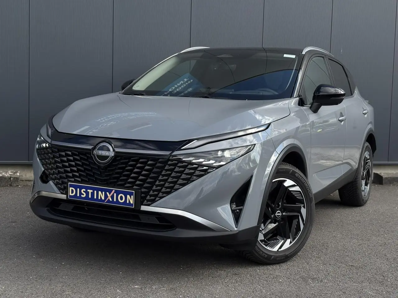 Nissan Qashqai gris Ceramic en 3/4 avant droit, avec calandre noire distinctive et jantes alliage 18 pouces bicolores.