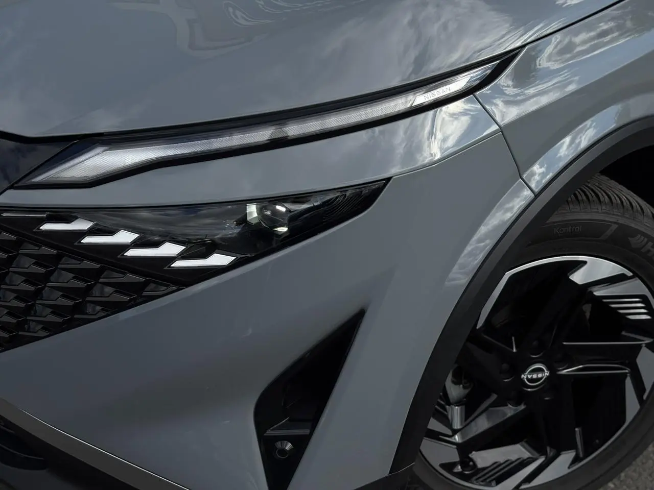 Gros plan sur l'avant droit gris Ceramic du Nissan Qashqai 2025, mettant en valeur le phare LED et la jante alliage noire.