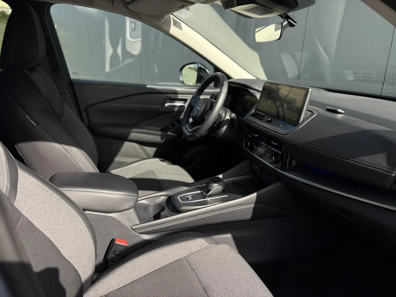Intérieur côté conducteur du Nissan Qashqai 2025, sellerie mixte noire, tableau de bord moderne avec écran tactile central.