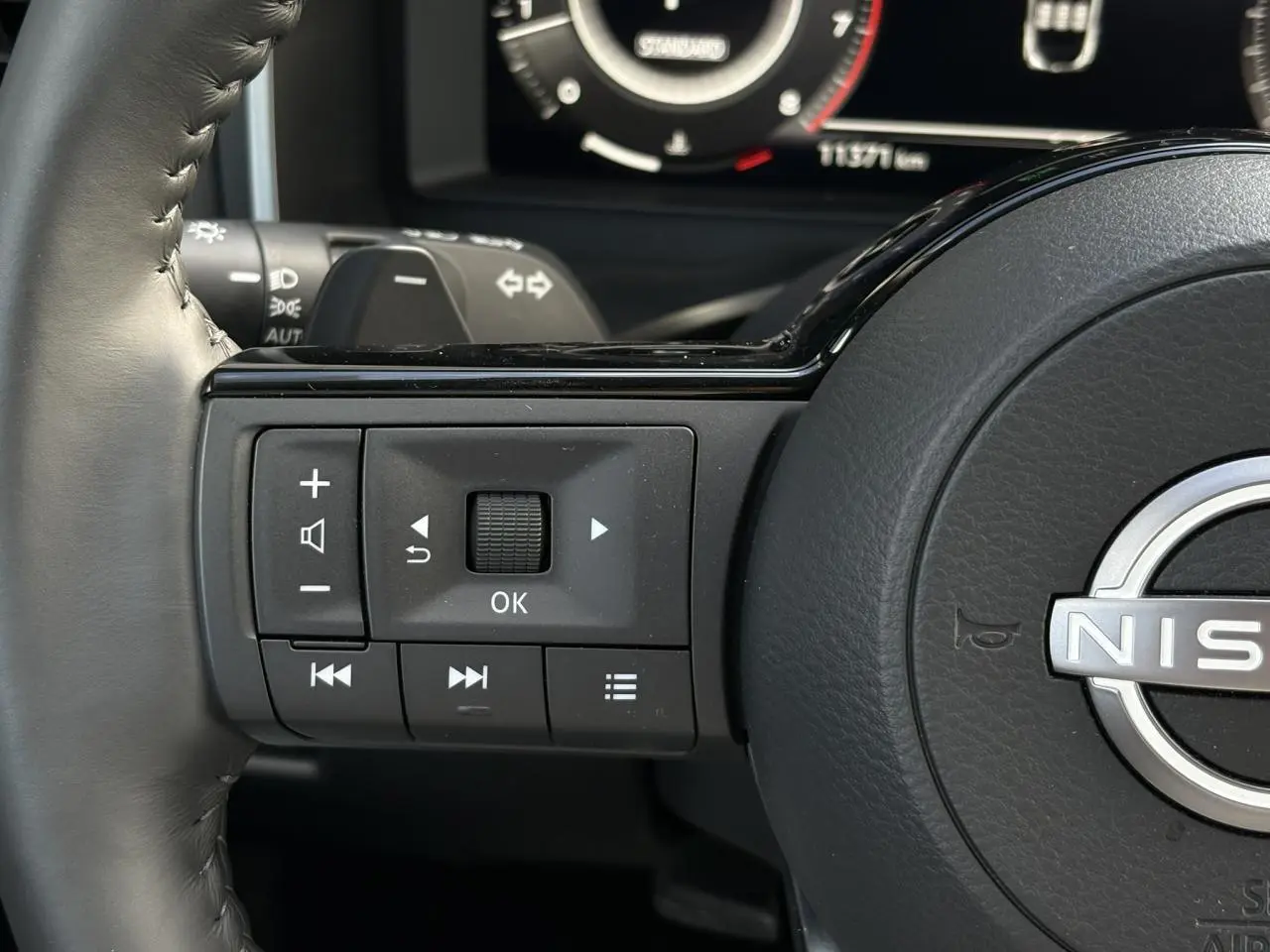 Gros plan sur les commandes au volant cuir noir du Nissan Qashqai 2025, avec affichage numérique en arrière-plan.