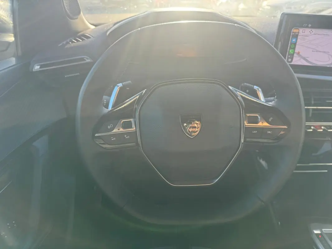 Vue rapprochée du volant noir du Peugeot 2008 Hybrid 136 e-DCS6 Allure 2024 avec commandes intégrées et écran tactile visible.