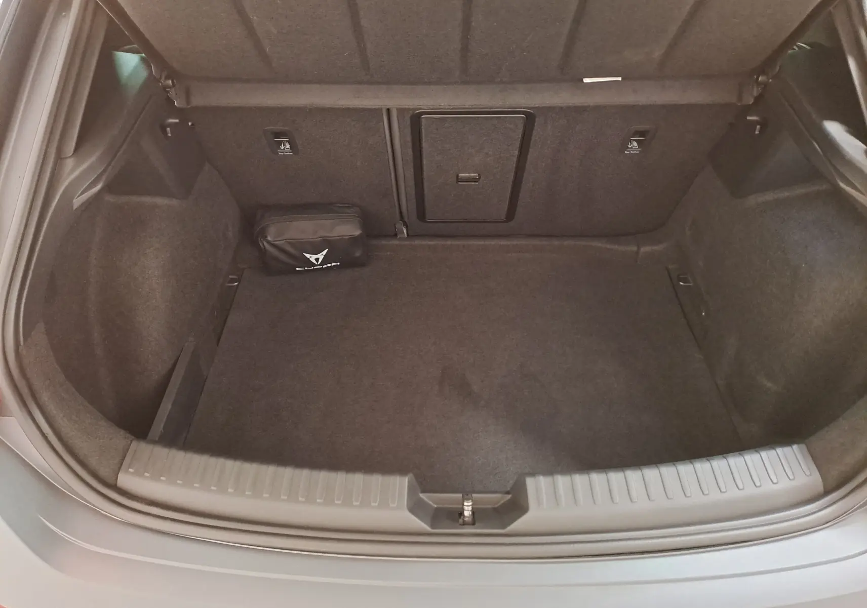 Coffre ouvert vu de dessus d'une CUPRA Leon 2024 gris magnétique mat avec trappe centrale et pochette noire CUPRA.