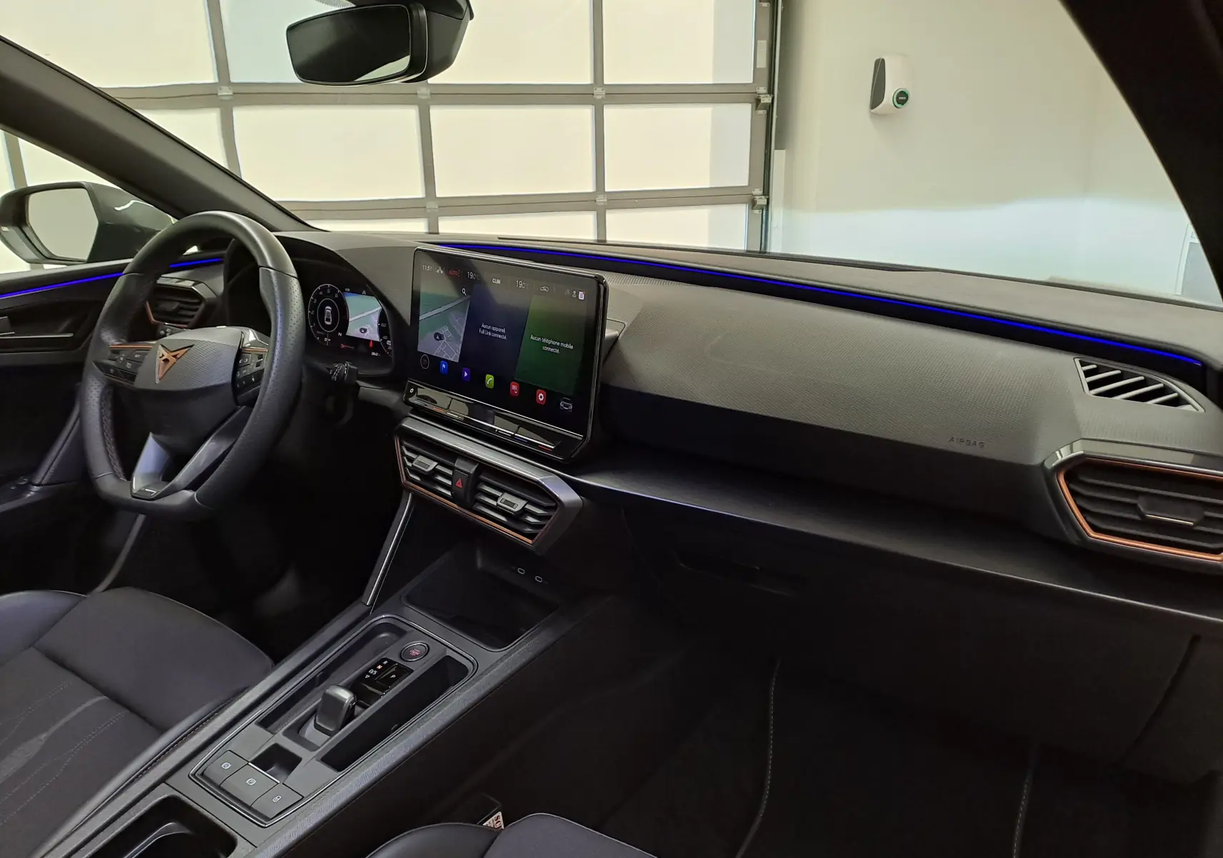 Vue intérieure côté conducteur du tableau de bord et console centrale du CUPRA Leon 2024 avec éclairage d'ambiance bleu.