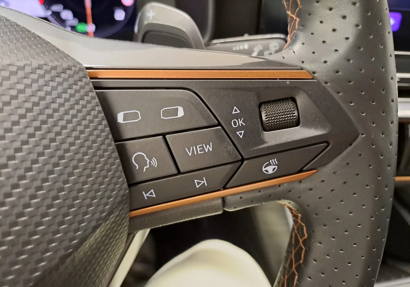 Gros plan sur les commandes à droite du volant perforé noir avec surpiqûres orange de la CUPRA Leon 2024.