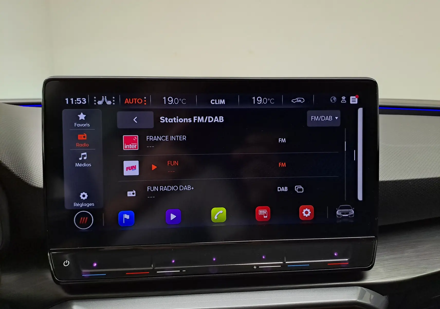 Écran tactile central de la CUPRA Leon 2024 affichant les stations FM/DAB avec interface moderne et commandes climatiques intégrées.
