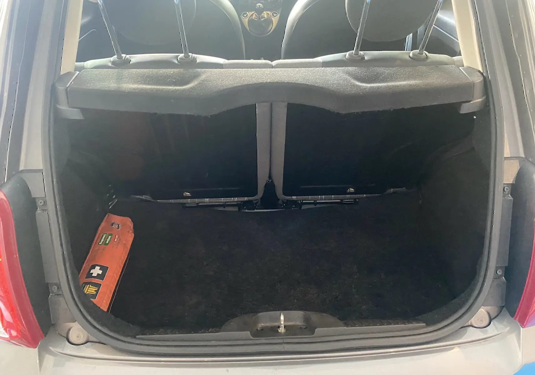 Vue du coffre ouvert d'une FIAT 500 gris foncé, montrant l'intérieur vide avec un kit de secours orange sur le côté gauche.