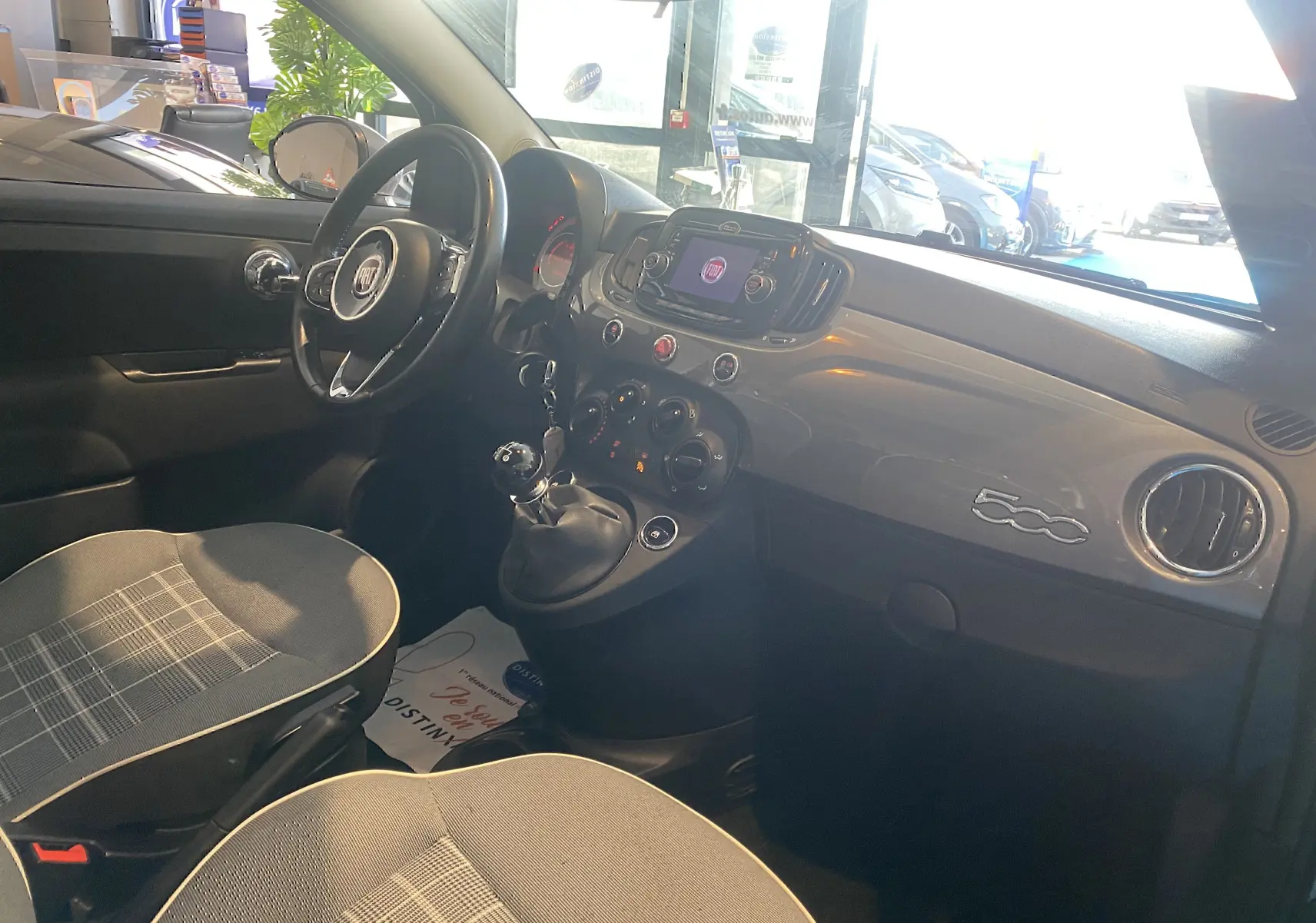 Intérieur gris foncé de la Fiat 500 Lounge 2019 vu côté conducteur, tableau de bord brillant avec logo 500 et levier de vitesse manuel.