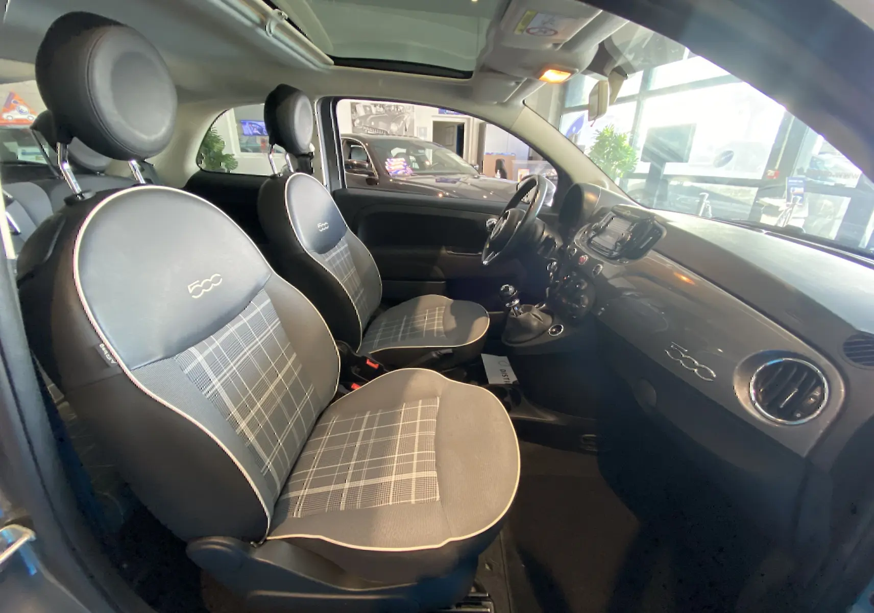 Vue intérieure côté gauche de la Fiat 500 Lounge 2019 gris foncé, sièges tissu à motifs et tableau de bord brillant.