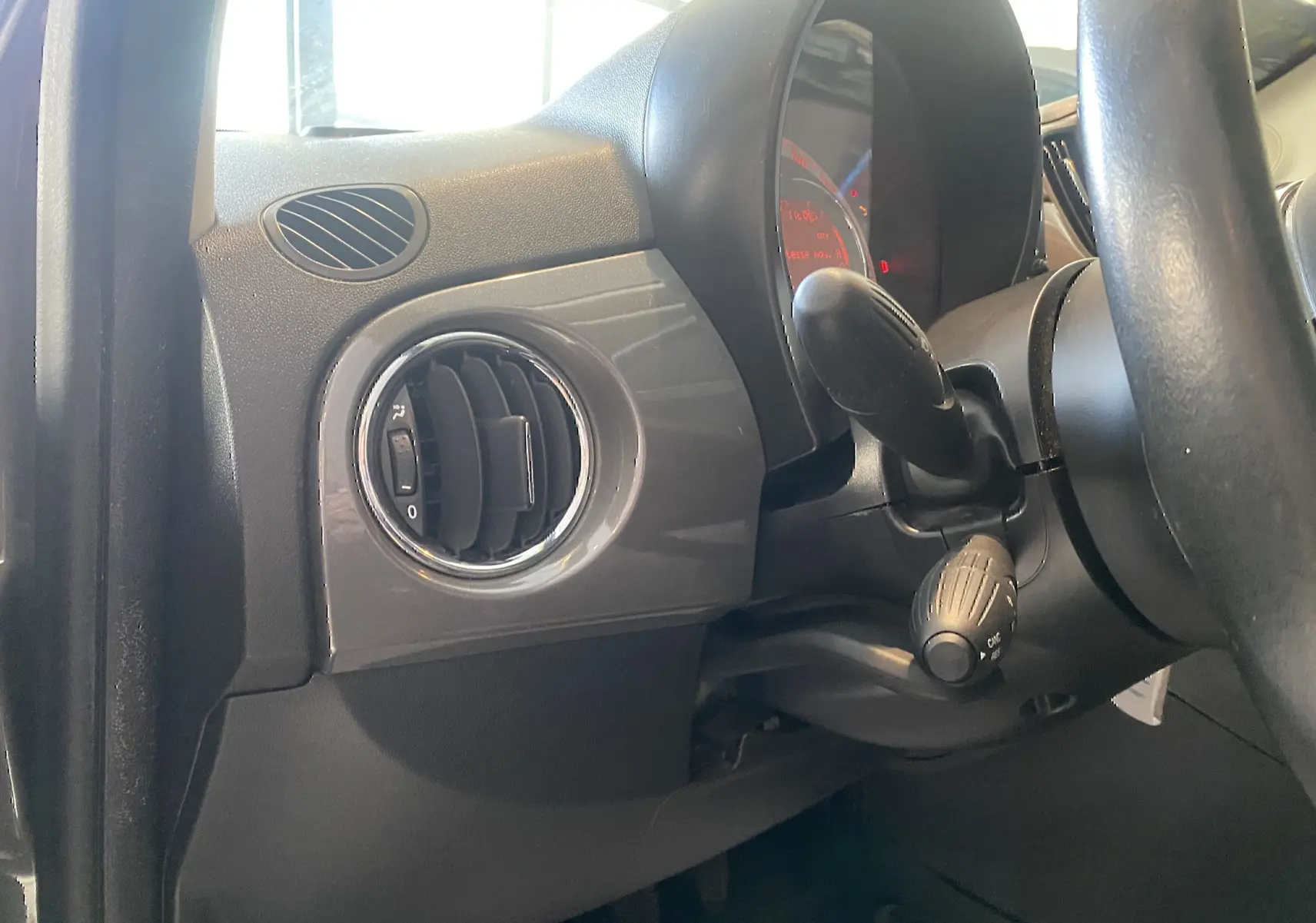Détail de la console côté gauche avec sortie d’air ronde et commandes du volant d’une Fiat 500 Lounge gris foncé de 2019.