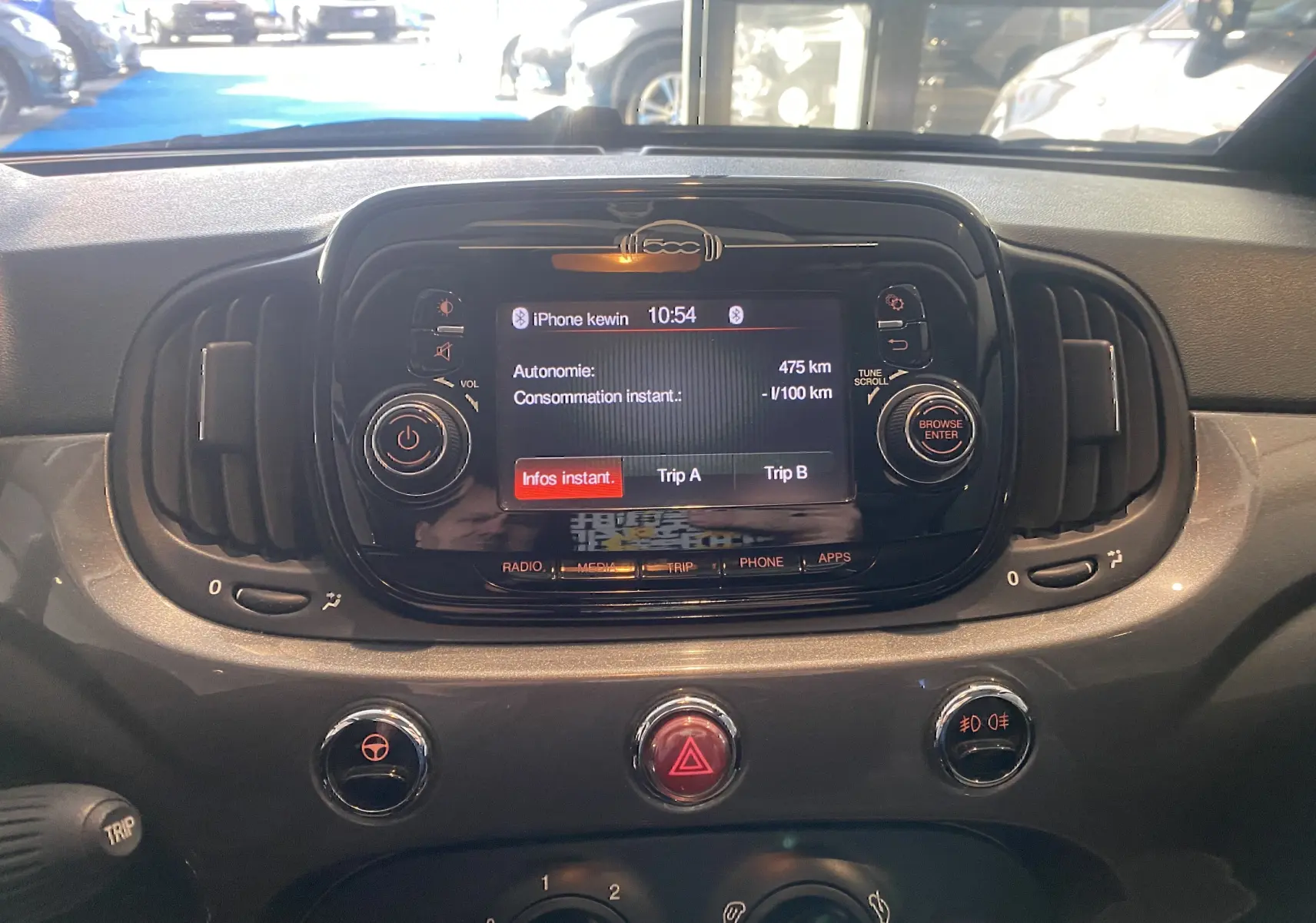 Vue rapprochée du tableau de bord noir de la Fiat 500 2019, avec écran central affichant l'autonomie et commandes autour.