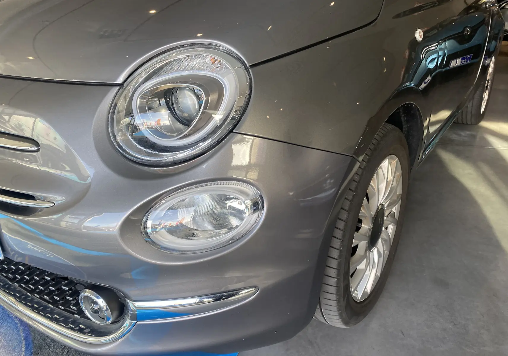 Gros plan sur l'avant droit d'une FIAT 500 gris foncé, mettant en valeur ses phares ronds et sa roue alu.