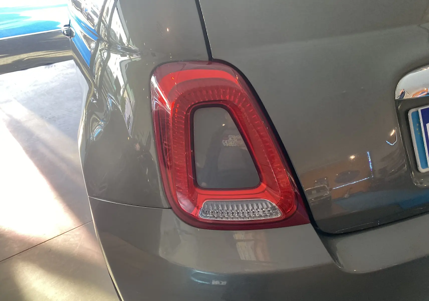 Gros plan sur le feu arrière gauche d'une Fiat 500 gris foncé, avec reflet lumineux sur la carrosserie.