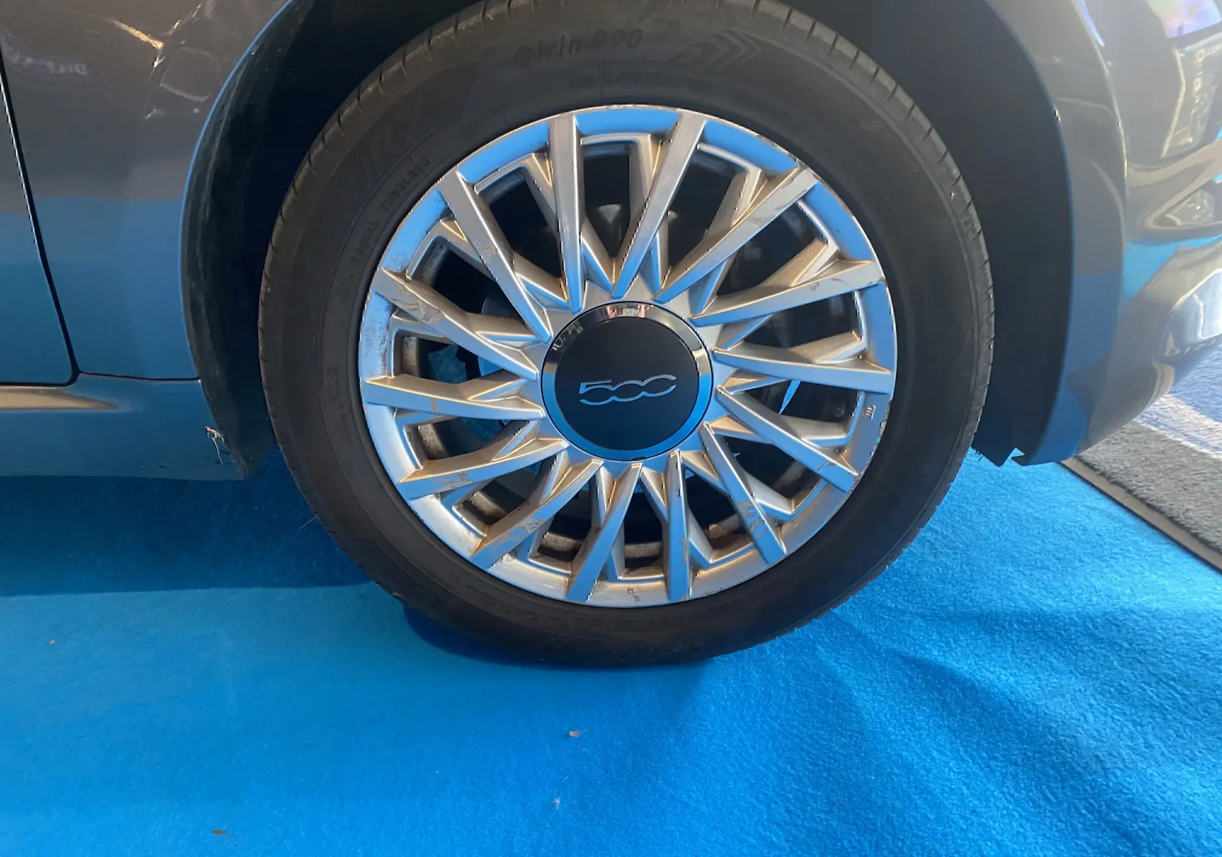 Gros plan sur la roue avant droite d'une Fiat 500 gris foncé avec jante alliage au design étoilé.