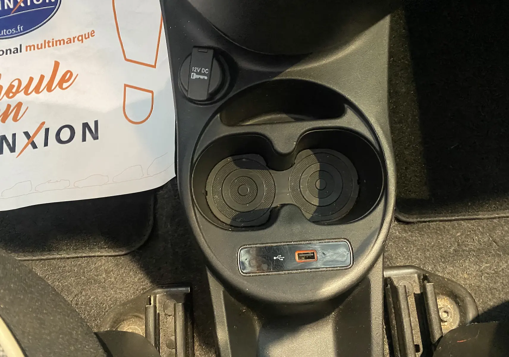 Gros plan sur la console centrale noire d'une Fiat 500 gris foncé, montrant porte-gobelets et prise USB.
