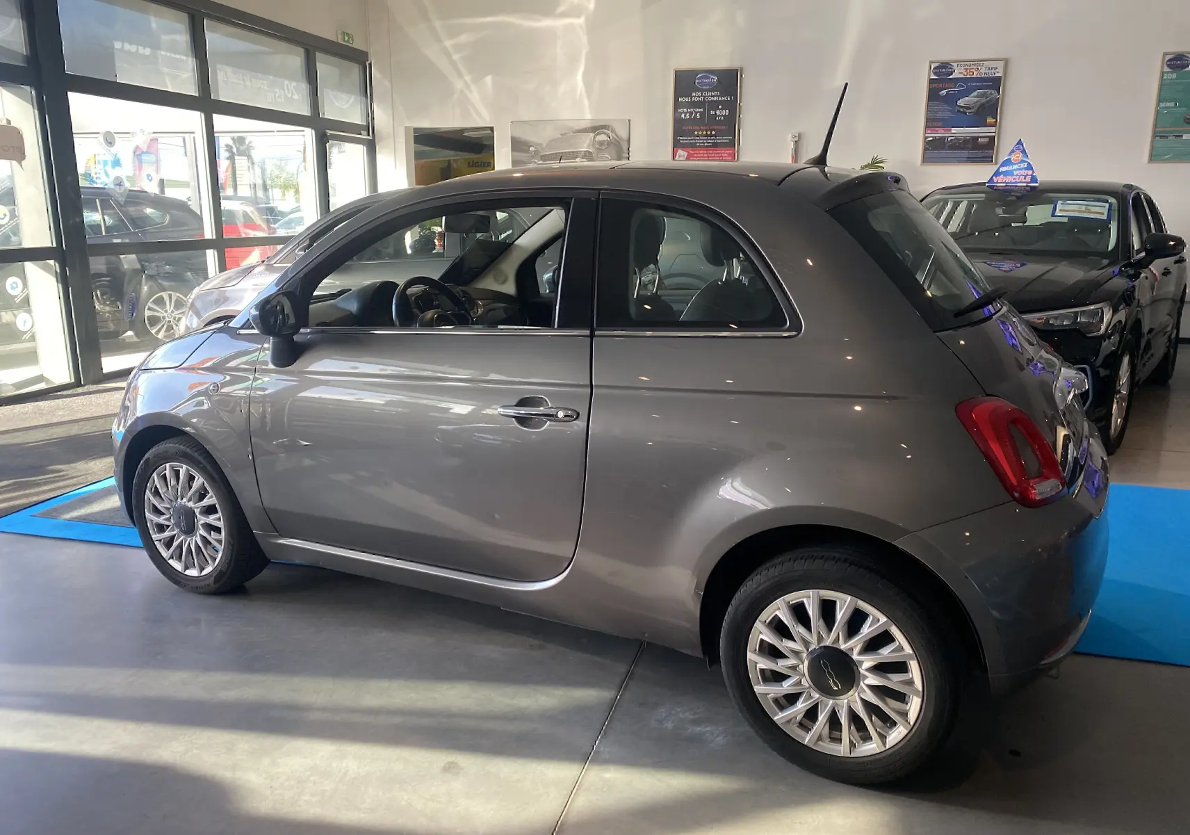 Profil droit d'une FIAT 500 gris foncé 2019 en showroom, avec jantes alliage et antenne de toit visible.
