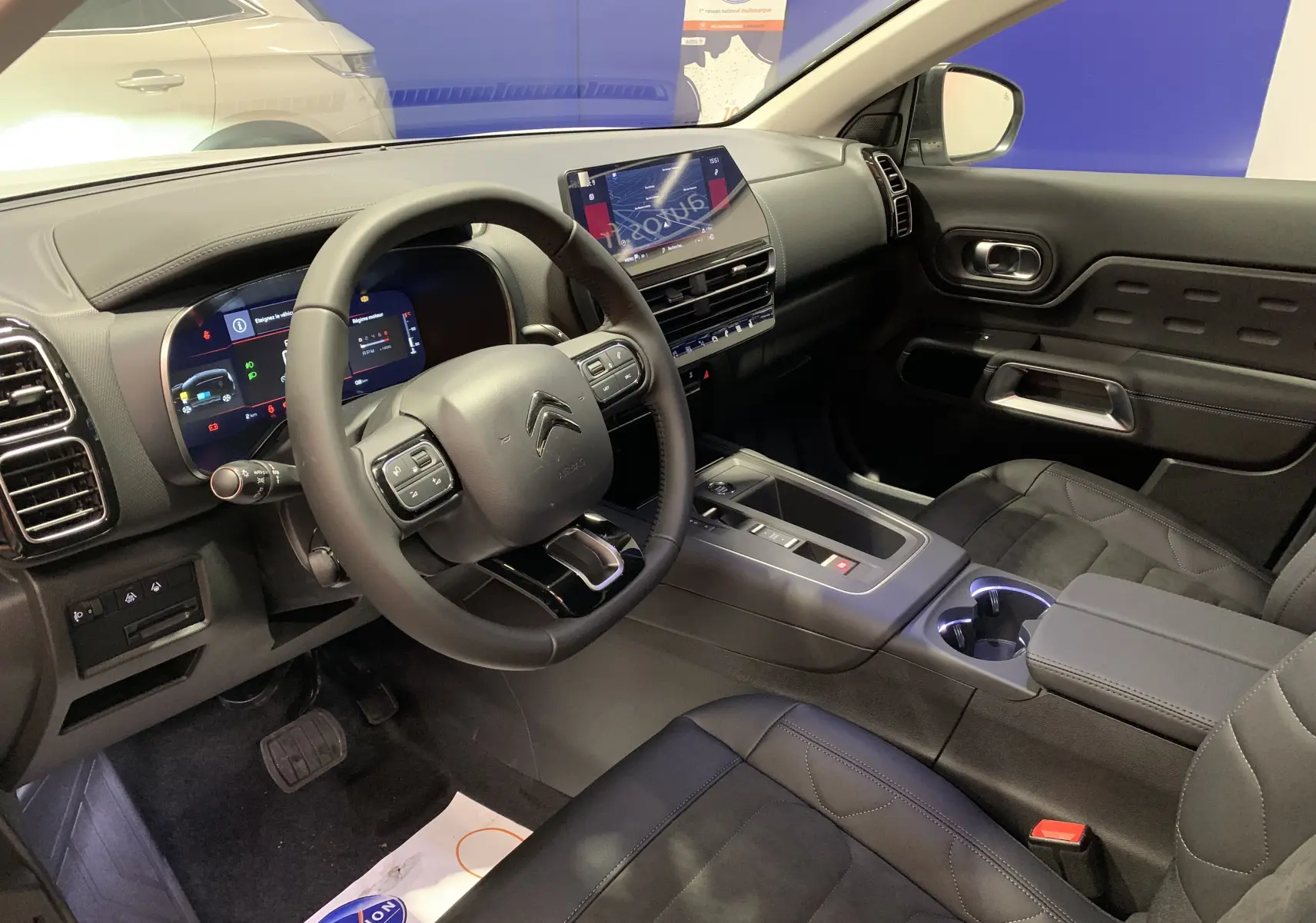 Vue intérieure côté conducteur du Citroën C5 Aircross hybride 2024, sièges en cuir noir avec surpiqûres bleues et tableau de bord moderne.