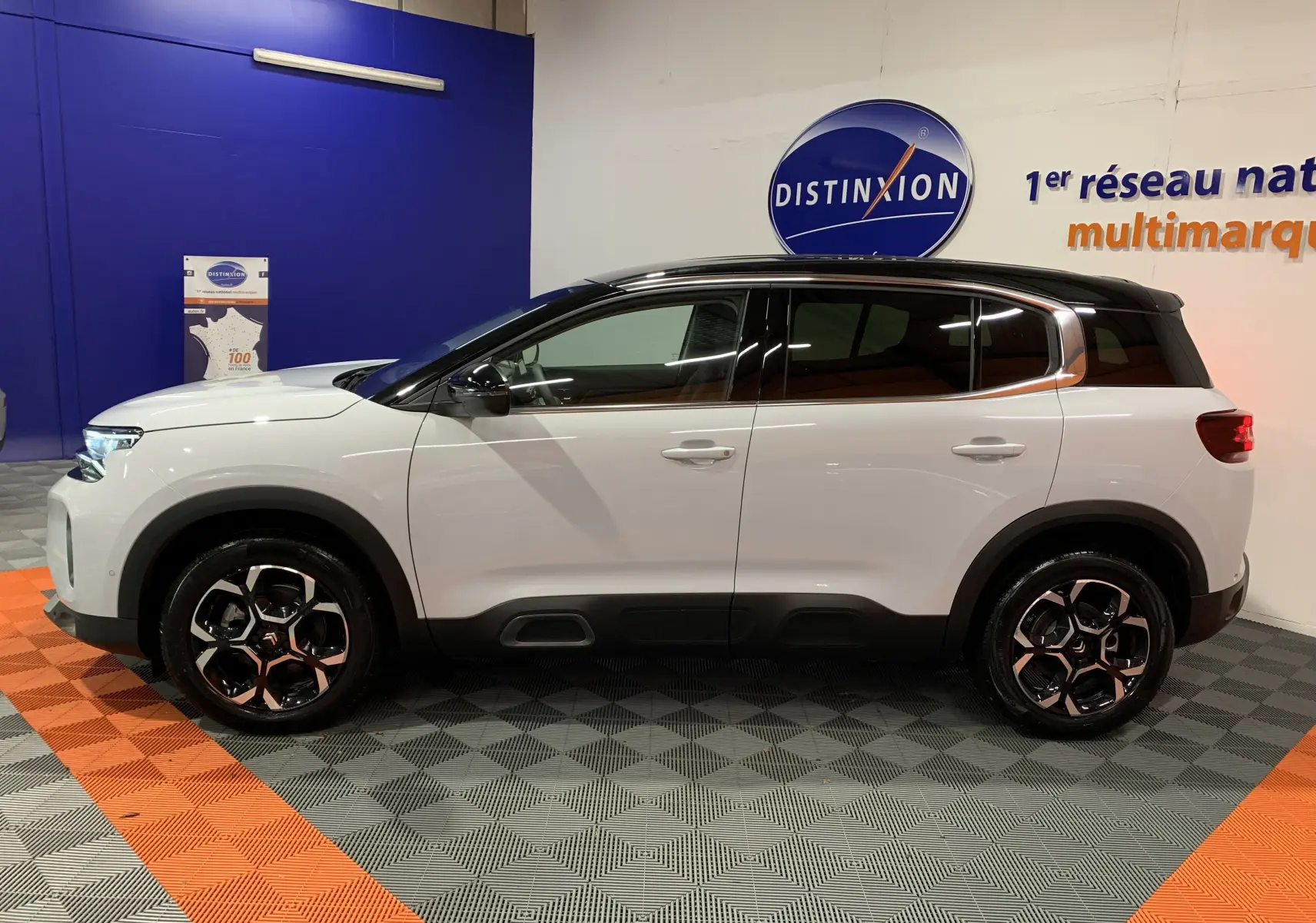 Profil côté gauche d'un Citroën C5 Aircross hybride blanc avec toit noir et jantes bicolores en showroom.