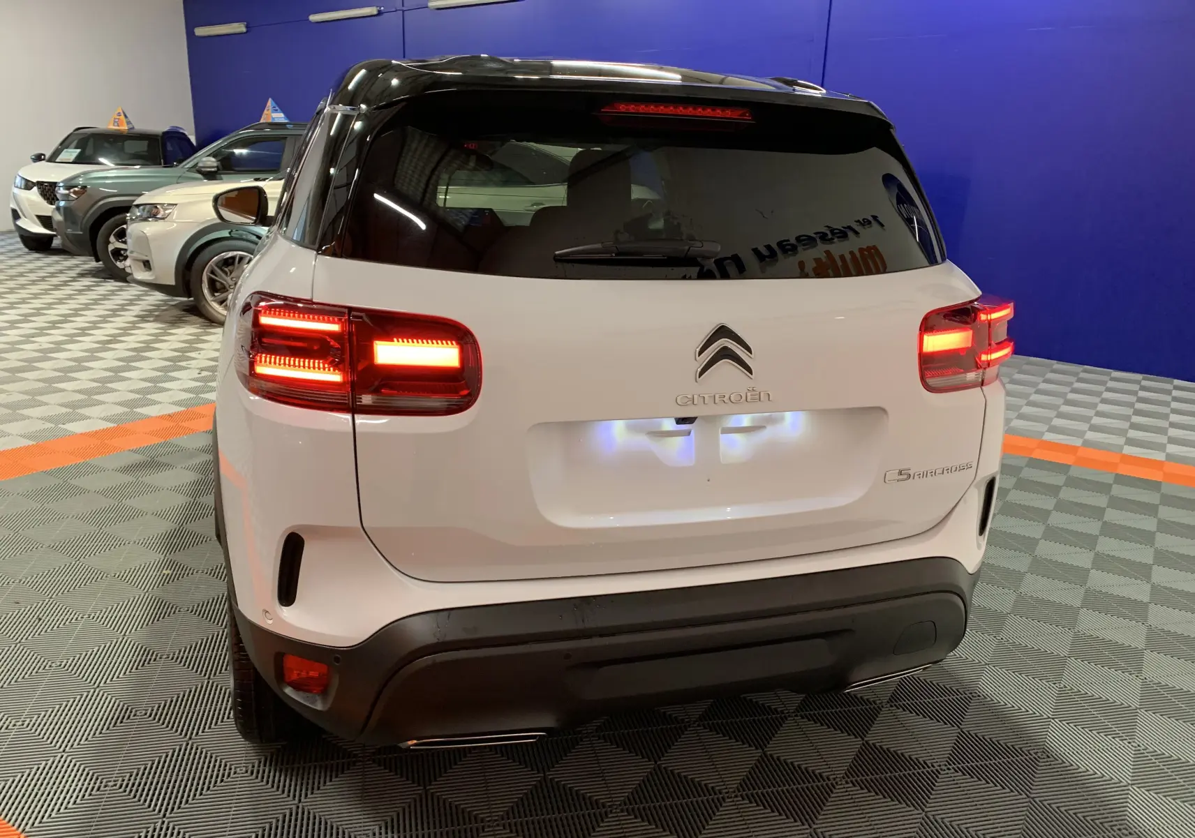 Vue arrière d'un Citroën C5 Aircross hybride blanc 2024 avec feux allumés dans un showroom.