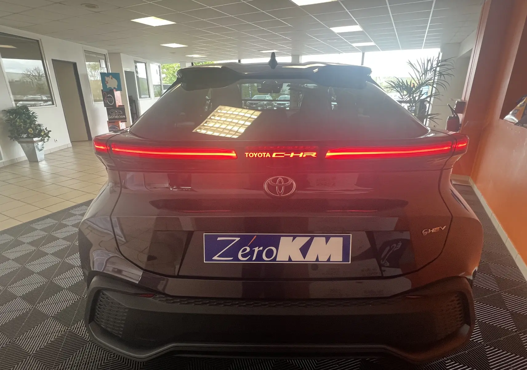 Vue arrière du Toyota C-HR 1.8 Hybrid 2024 en améthyste métal avec feux LED horizontaux allumés en intérieur showroom.