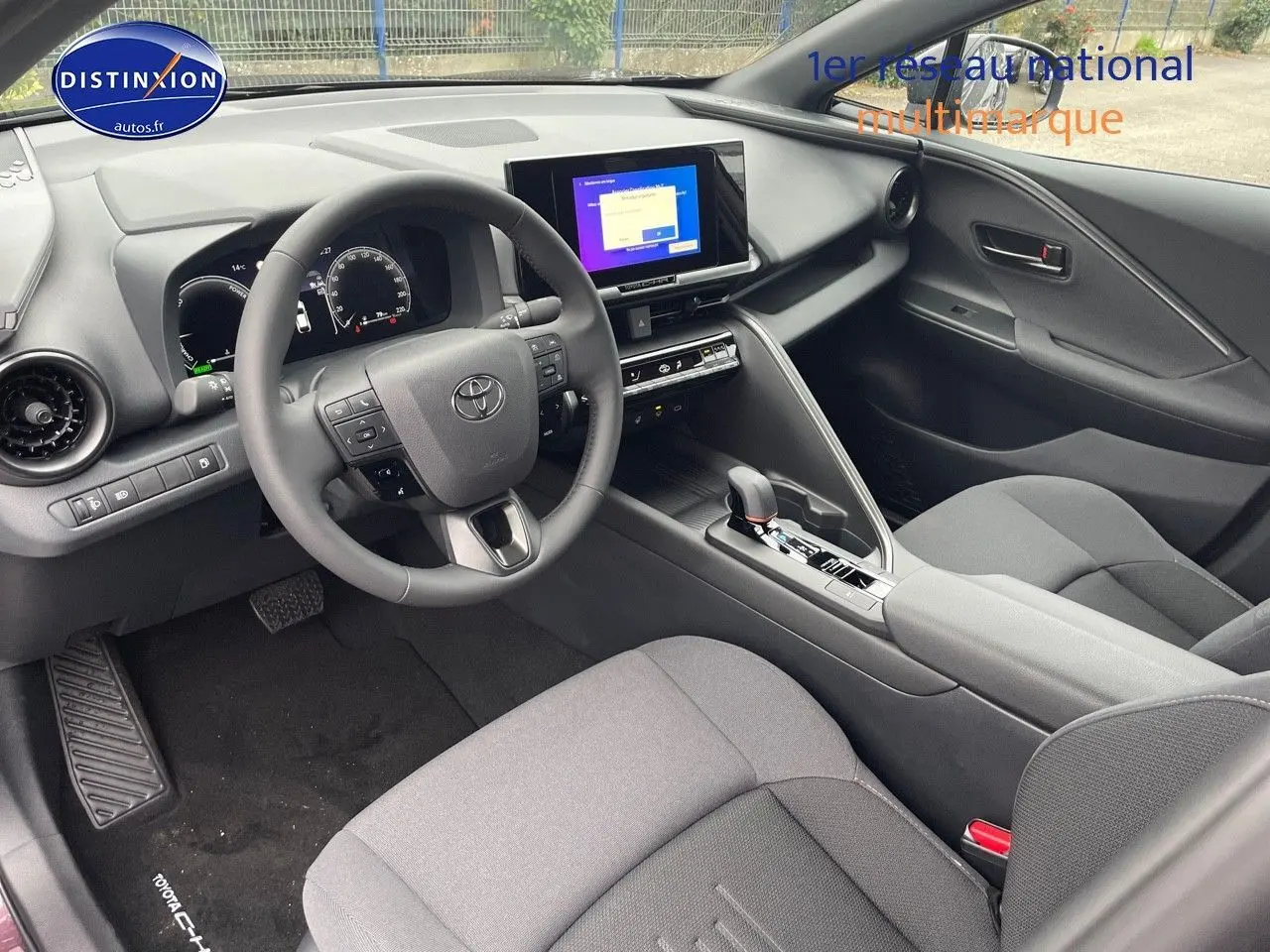 Vue intérieure côté conducteur du Toyota C-HR 1.8 Hybrid 2024 avec tableau de bord moderne et sièges gris foncé.