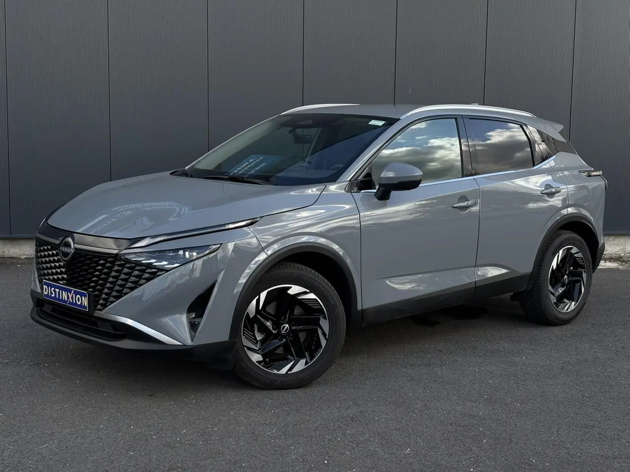 Nissan Qashqai 2025 gris Ceramic en 3/4 avant droit avec jantes alliage noires et calandre distinctive.