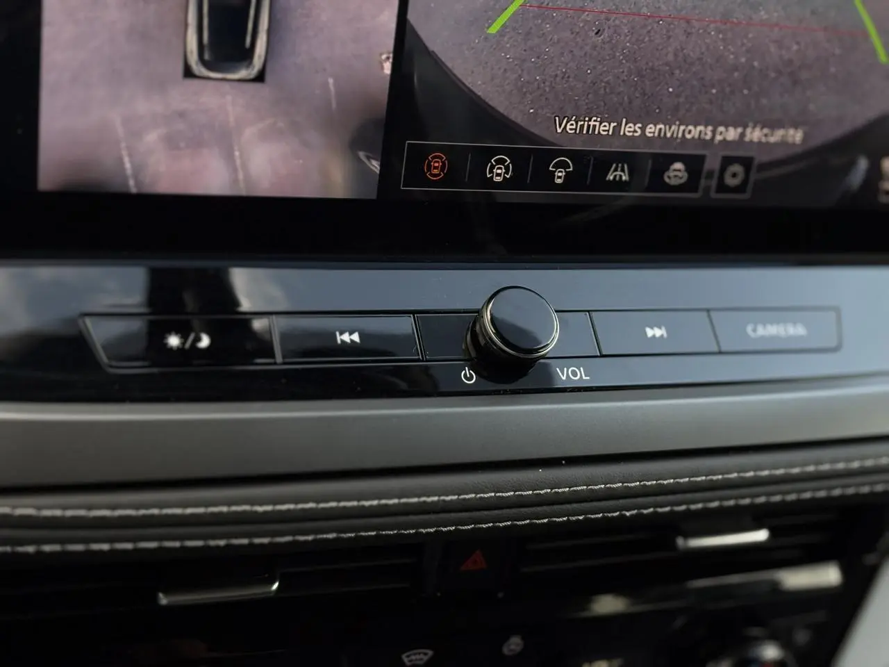 Gros plan sur la console centrale du Nissan Qashqai 2025, boutons de volume et caméra avec écran tactile visible.
