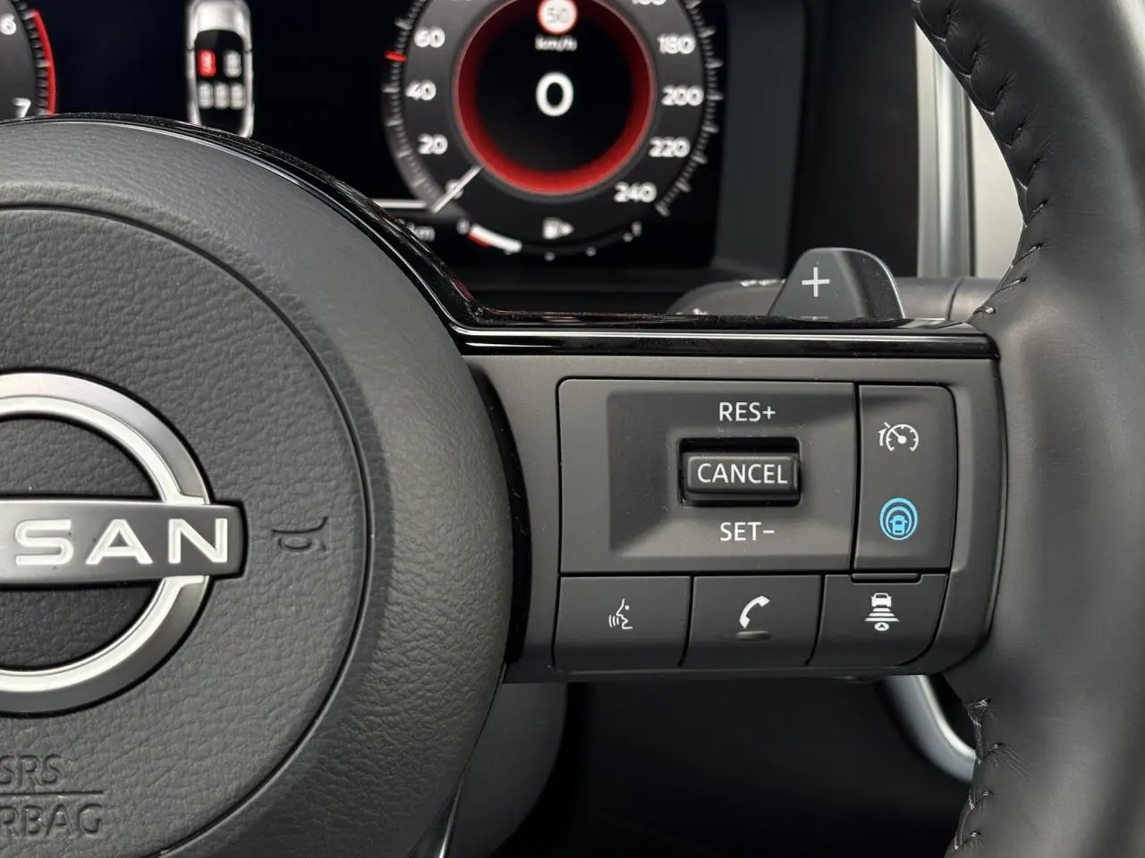 Gros plan sur le volant cuir noir du Nissan Qashqai 2025, avec commandes de régulateur et affichage numérique en arrière-plan.