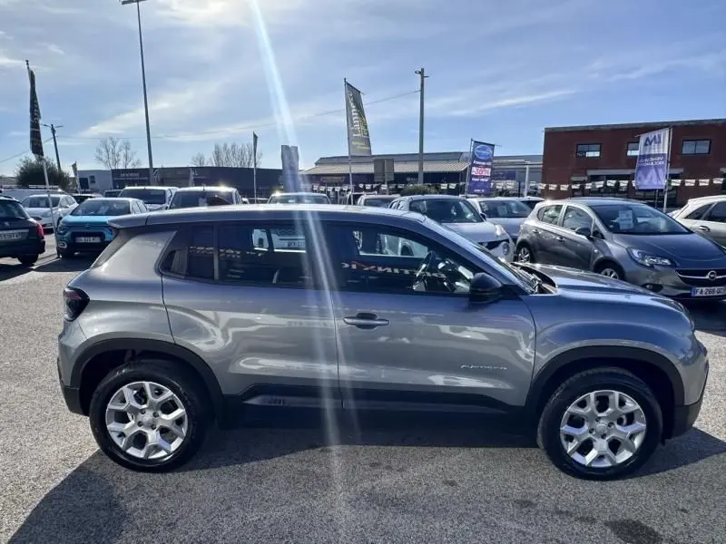 Vue de profil côté gauche d’un Jeep Avenger 2025 gris métallisé avec jantes alliage et toit noir en extérieur.