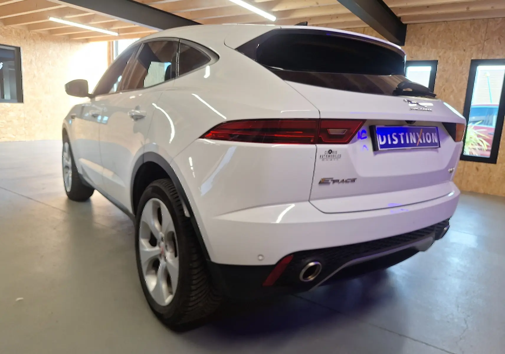 Vue 3/4 arrière gauche d'un Jaguar E-PACE blanc avec feux arrière LED et sortie d'échappement chromée dans un garage.