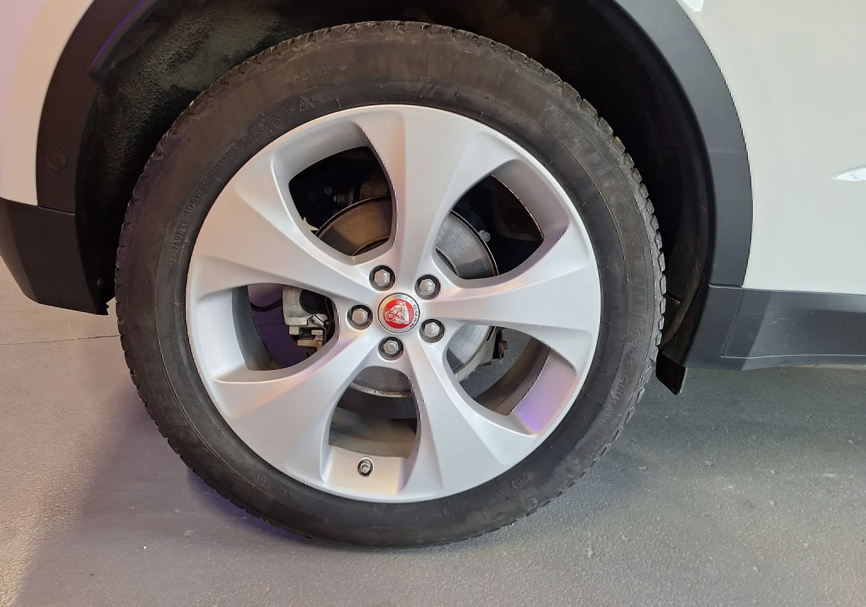 Gros plan sur la roue avant droite d'un Jaguar E-PACE blanc avec jante argentée et logo Jaguar rouge au centre.