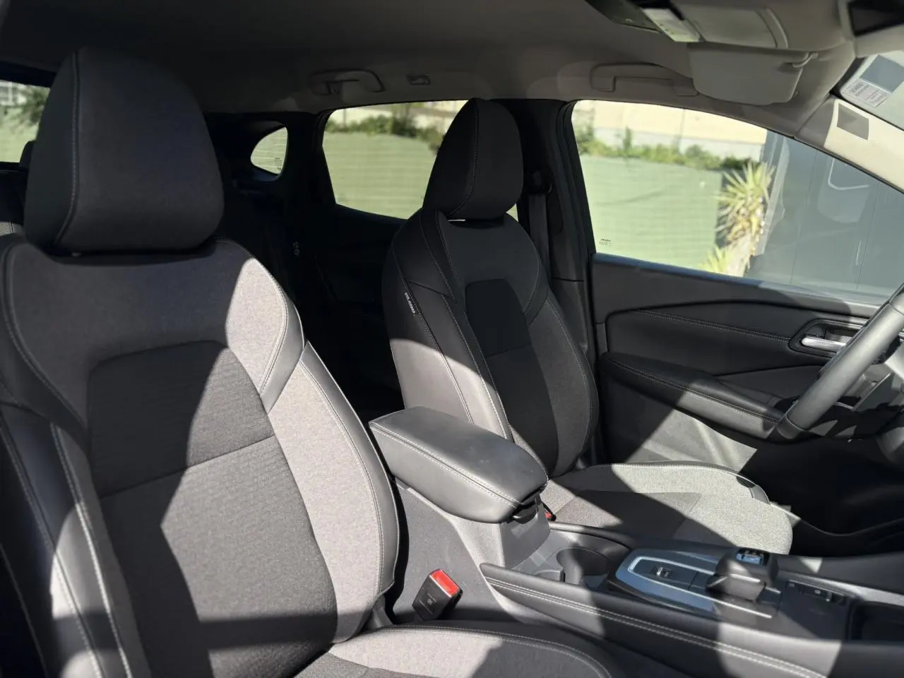 Intérieur du Nissan Qashqai 2025 montrant les sièges avant gris et la console centrale avec accoudoir et levier de boîte automatique.