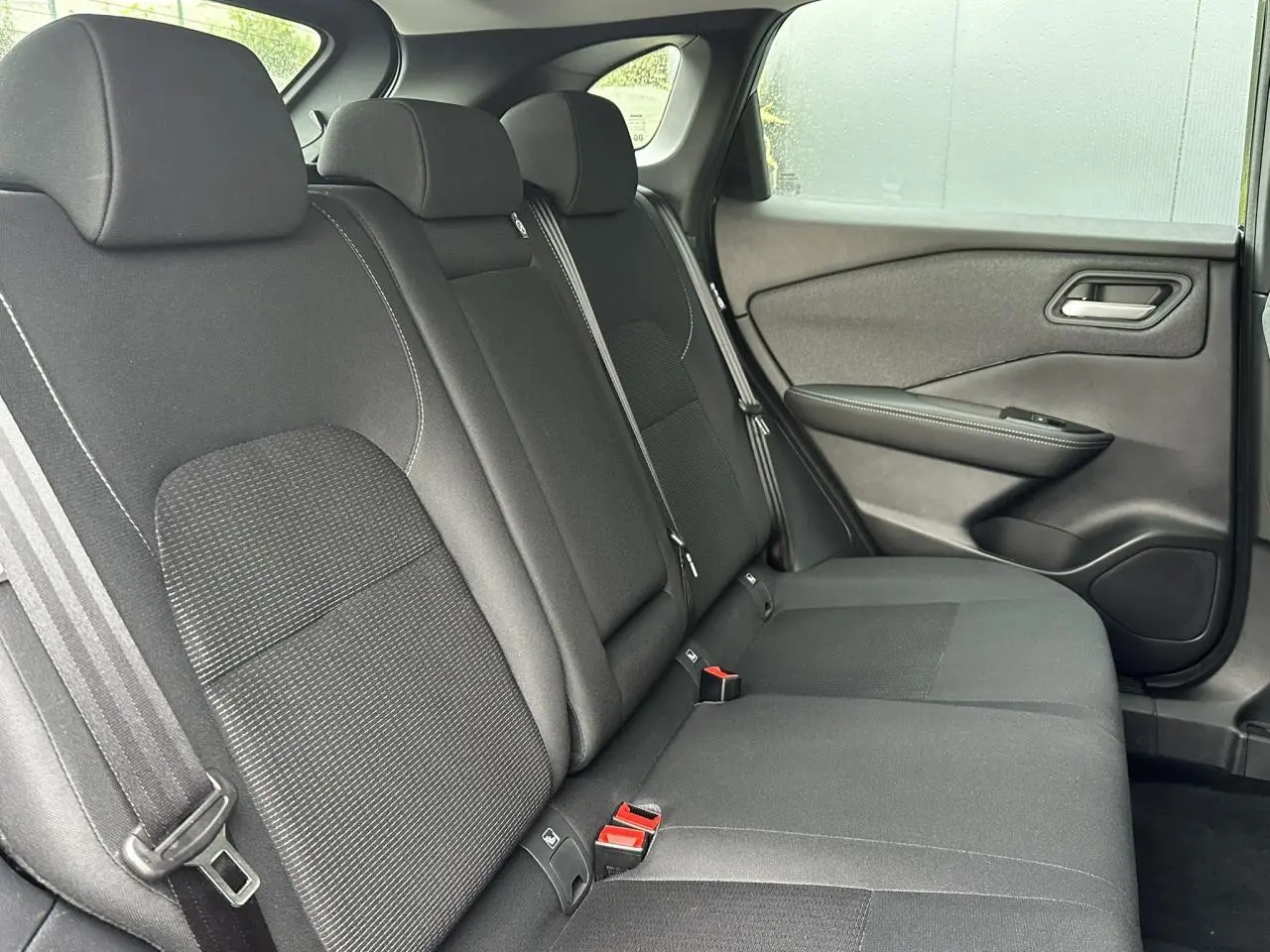 Vue latérale des sièges arrière noirs du Nissan Qashqai 2024, montrant la porte côté droit et les ceintures de sécurité.