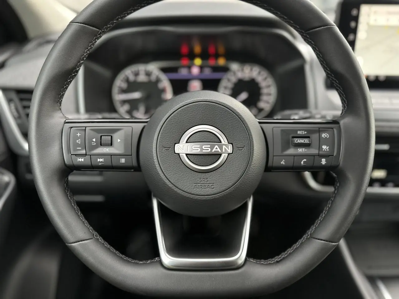Vue rapprochée du volant en cuir noir du Nissan Qashqai 2024 avec commandes intégrées et tableau de bord flou en arrière-plan.
