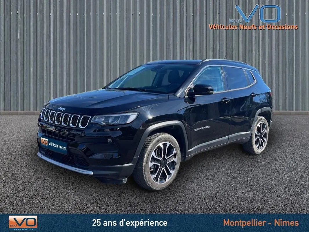 Jeep Compass noir en 3/4 avant droit, avec barres de toit et jantes 18 pouces visibles sur fond industriel.