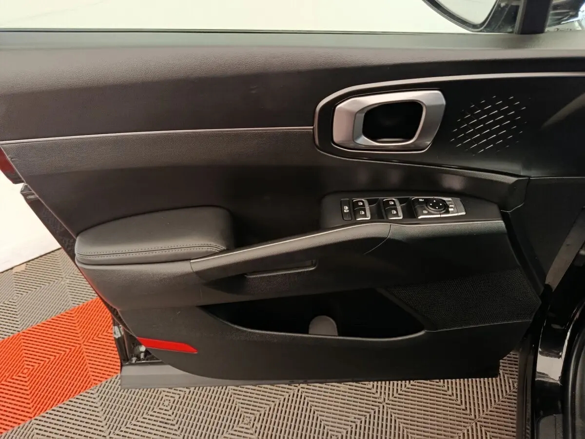 Vue intérieure côté gauche de la porte avant noire du Kia Sorento 2023 avec commandes électriques et poignée argentée.