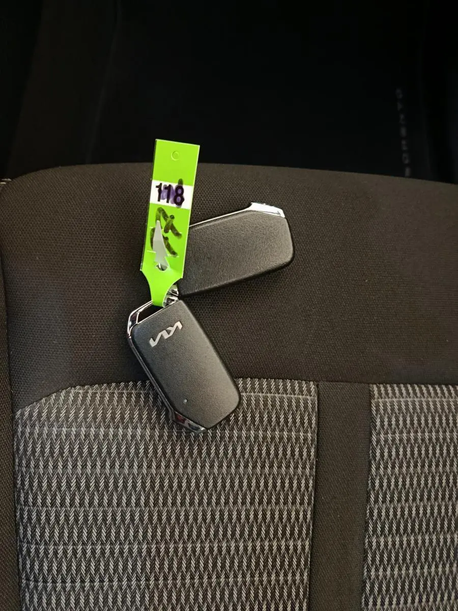 Clé noire KIA posée sur siège tissu gris à motifs, vue rapprochée sans angle de véhicule visible.