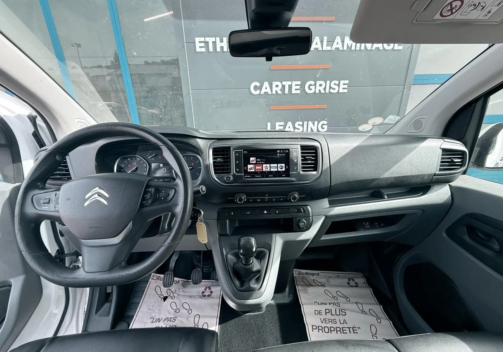Vue intérieure avant du Citroën Jumpy blanc 2017, tableau de bord avec volant, écran central et boîte manuelle.