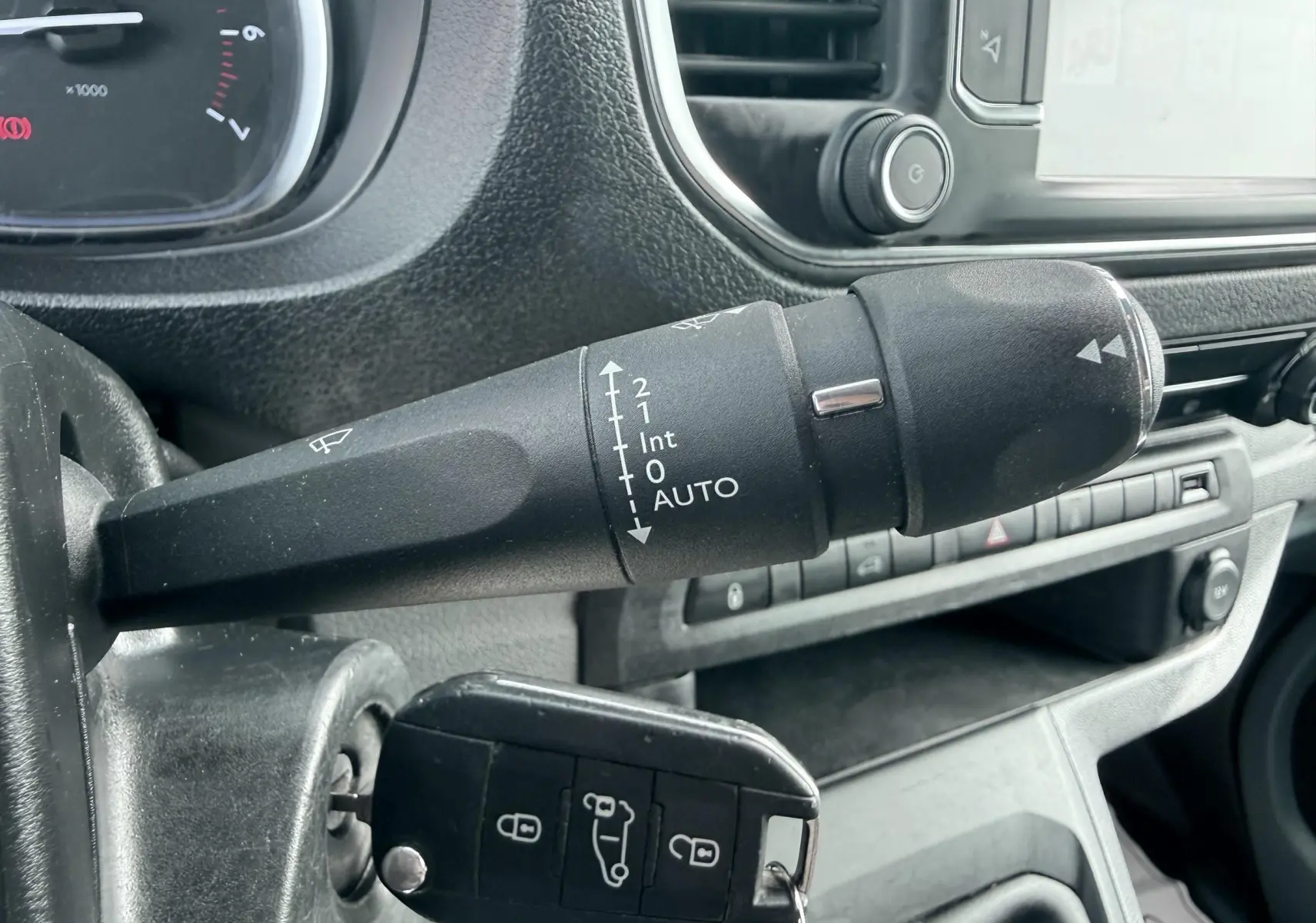 Gros plan sur la commande d’essuie-glace noire et la clé insérée dans le contact d’un Citroën Jumpy blanc, intérieur gris.