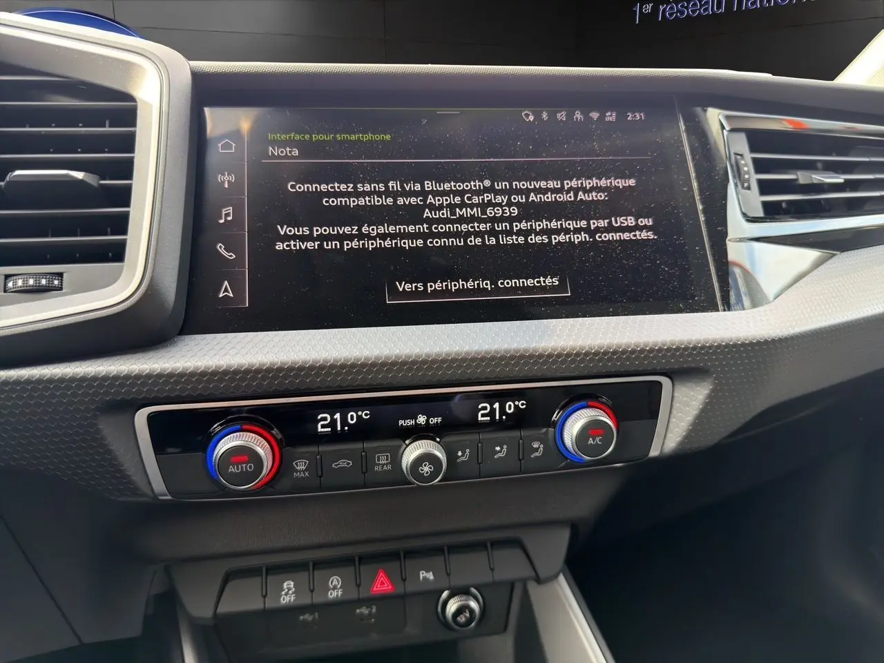 Vue rapprochée du tableau de bord de l'Audi A1 Sportback blanc 2025, mettant en valeur l'écran tactile et la climatisation bizone.