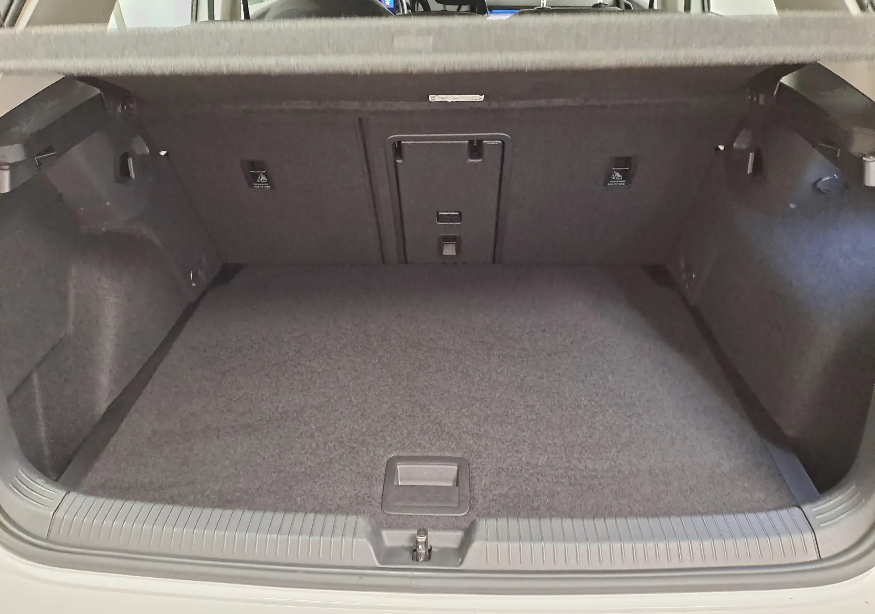 Coffre ouvert vu de l'arrière d'une Volkswagen Golf 1.5 TSI blanc pur, montrant un espace de chargement propre et spacieux.