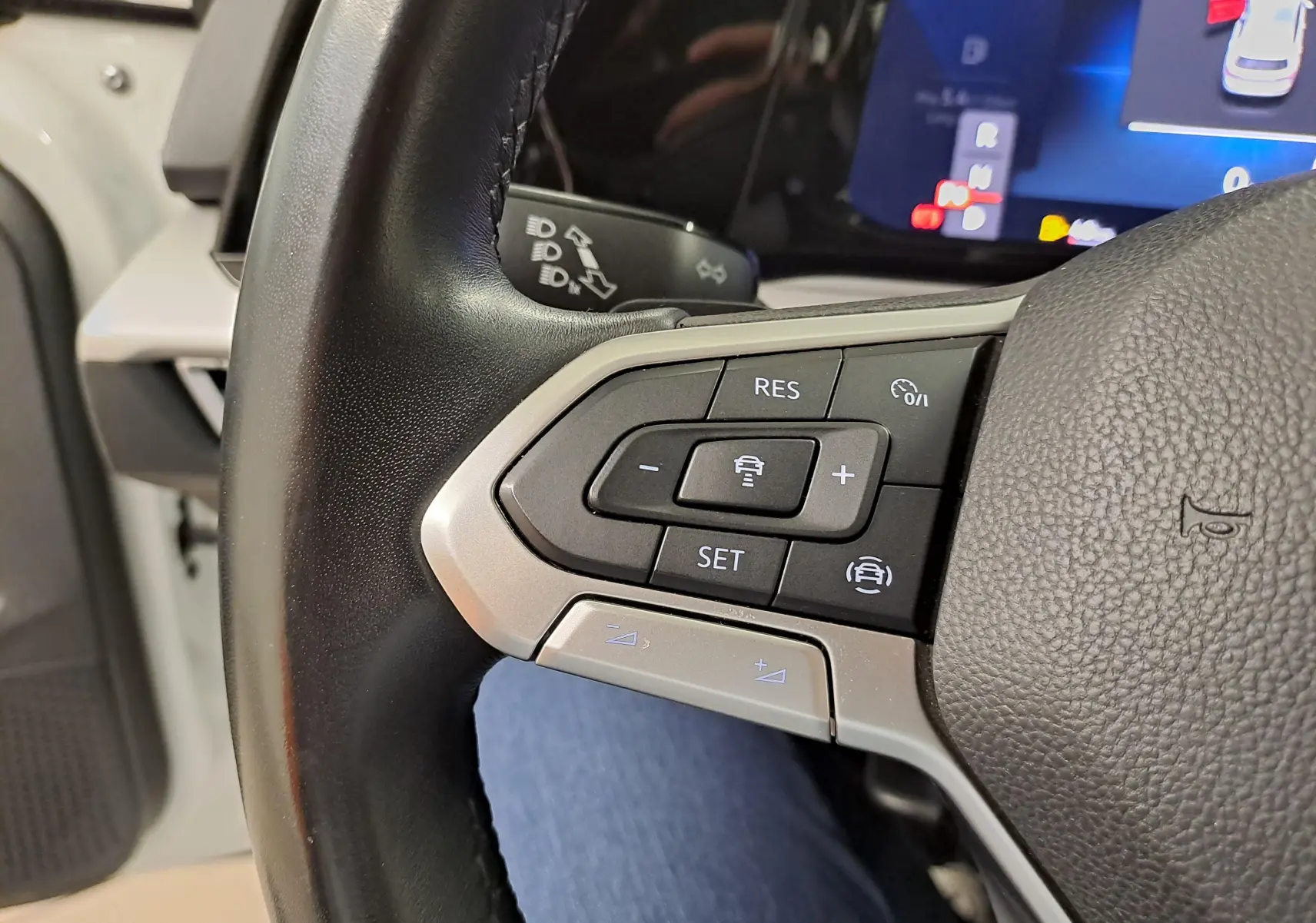 Gros plan sur les commandes au volant côté gauche d'une Volkswagen Golf blanche avec affichage digital au tableau de bord.