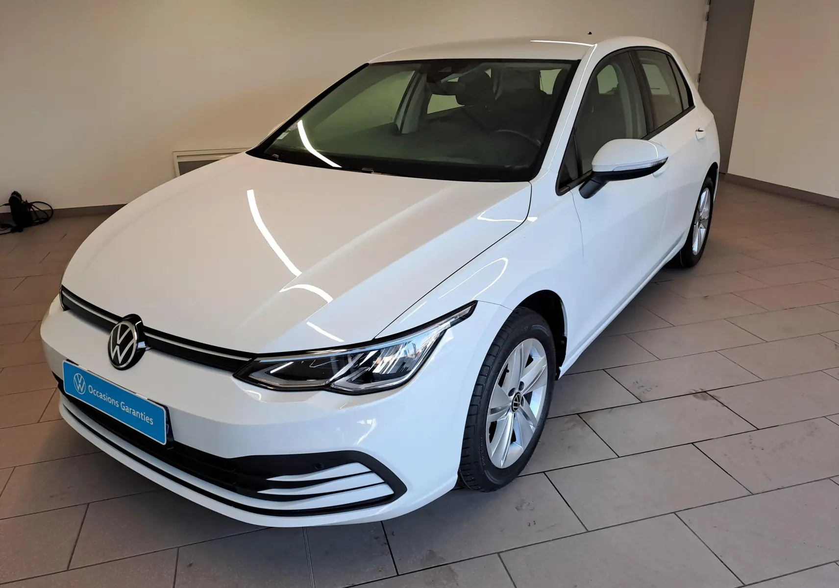 Volkswagen Golf blanc pur vue 3/4 avant droit dans un showroom, avec calandre noire et jantes alliage.