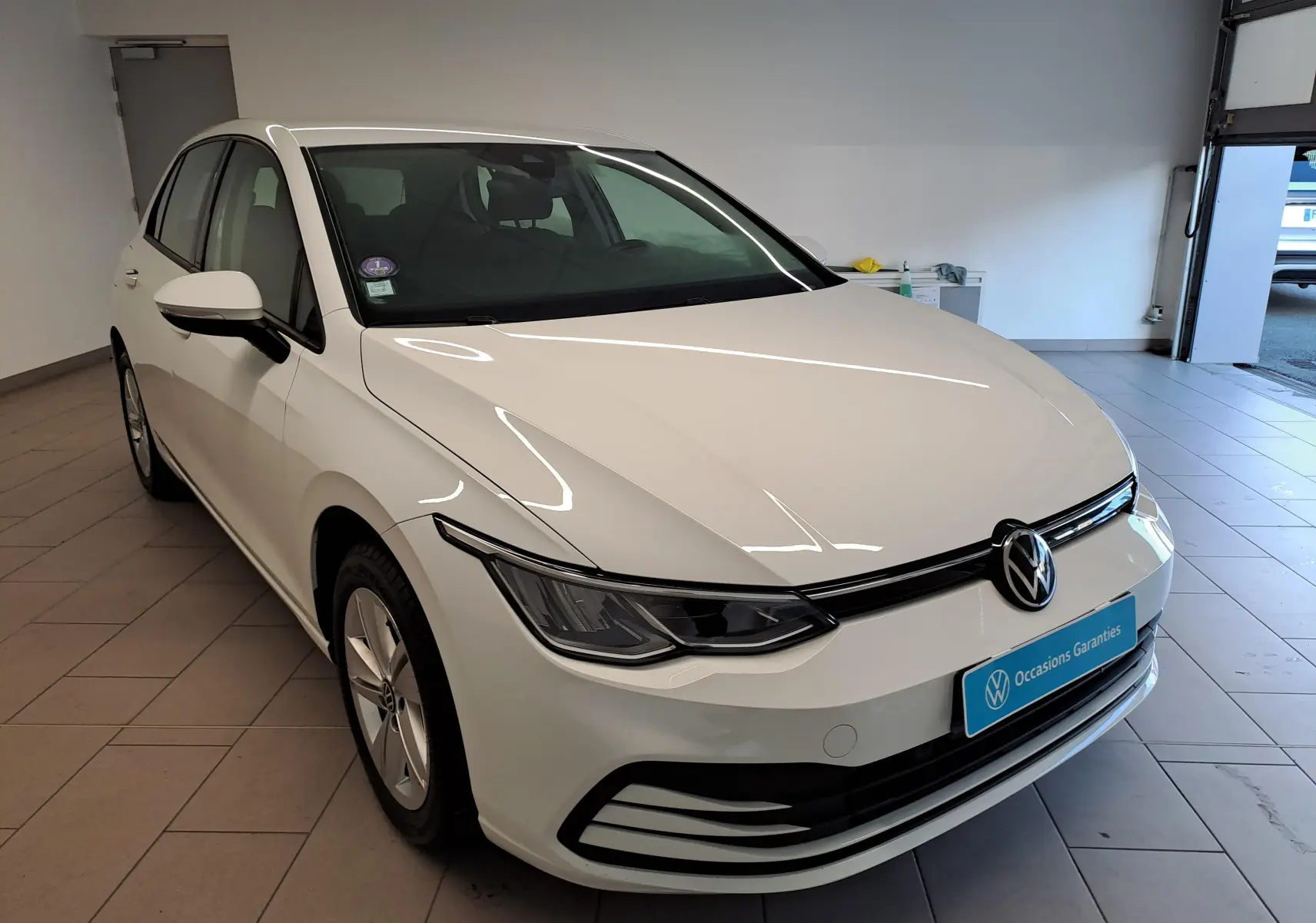 Volkswagen Golf blanc pur vue 3/4 avant droit en intérieur, avec calandre noire et phares LED fins.