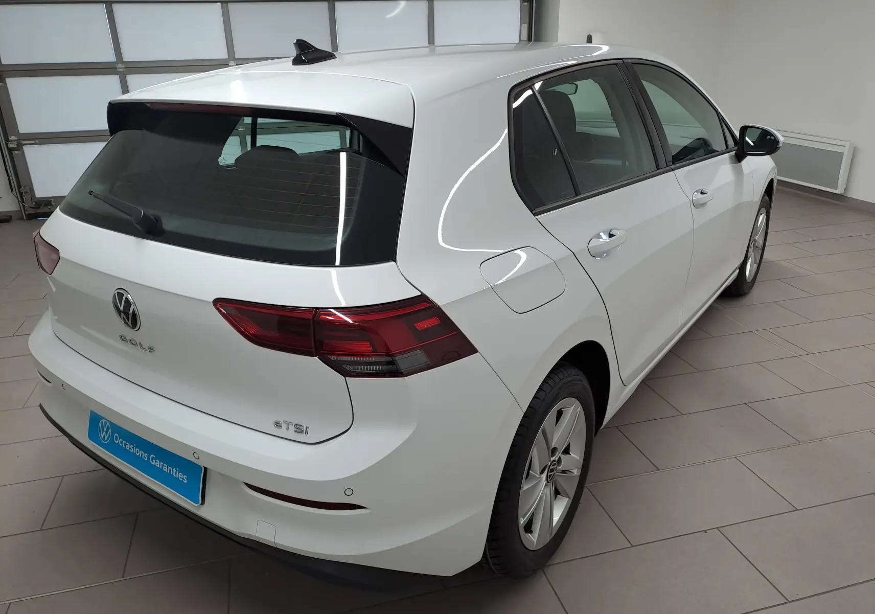 Volkswagen Golf blanc pur vue 3/4 arrière droit en intérieur avec caméra de recul visible sur le pare-chocs.
