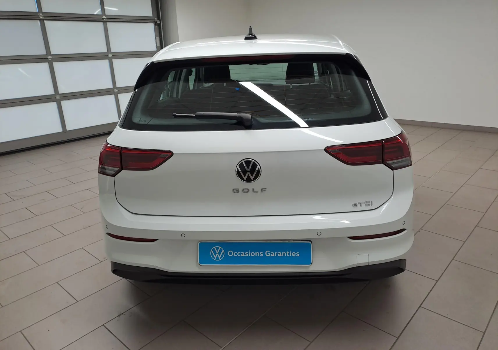Vue arrière d'une Volkswagen Golf blanche Pure avec logo et feux arrière LED, stationnée en intérieur.